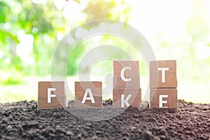 Fake news versus facts concept. Hand changing fake wooden blocks to word fact in natural background.