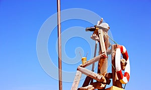 Fake wooden sailor sipping a drink under the blue sky and with a round white and red life buoy