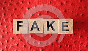 FAKE word written in wooden blocks on red leather. Fake or real news, myth or true concept