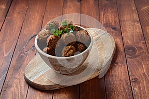 Falafel balls with parsley in wooden bowl with tahini sauce.