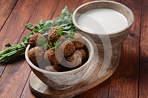 Falafel balls with parsley in wooden bowl with tahini sauce.