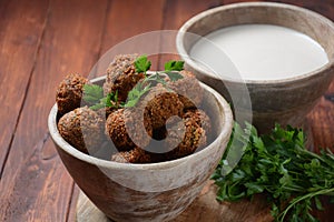 Falafel balls with parsley in wooden bowl with tahini sauce.