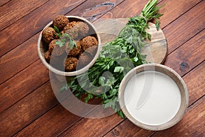 Falafel balls with parsley in wooden bowl with tahini sauce.