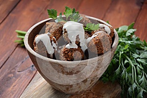 Falafel balls with parsley in wooden bowl with tahini sauce.