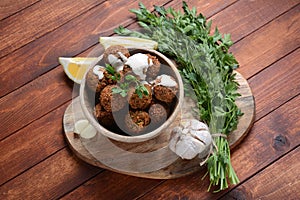 Falafel balls with parsley in wooden bowl with tahini sauce.