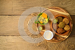 Falafel balls with tahini sauce on wooden board.