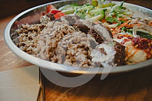 Falafel in a metallic bowl with raw fresh vegetables salad on a wooden table close up. Eating Jewish cuisine at a