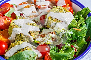 Falafel salad with baked vegetables, tahini dressing and tomatoes in white bowl. Israeli street food concept