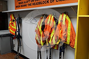 Fall arrest gear and orange high visibility safety vests hanging in the changing-room for stevedores using when aloft of container