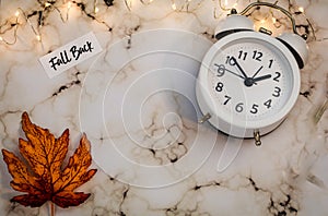 Fall Back Daylight Saving Time concept with white clock and autumn leaves