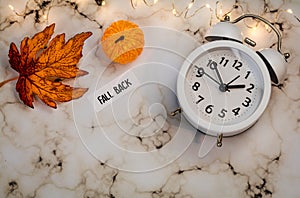 Fall Back Daylight Saving Time concept with white clock and autumn leaves