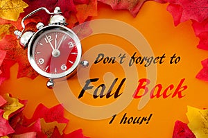 Fall back, the end of daylight savings time and turn clocks back on hour concept with a clock surrounded by dried yellow leaves