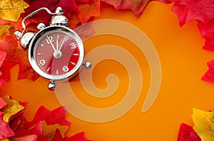 Fall back, the end of daylight savings time and turn clocks back on hour concept with a clock surrounded by dried yellow leaves