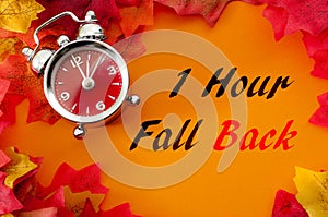 Fall back, the end of daylight savings time and turn clocks back on hour concept with a clock surrounded by dried yellow leaves