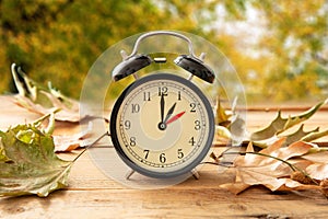 Fall Back one hour. Daylight Saving Time, Black clock on wood, autumn trees background