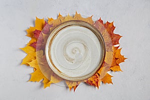Fall background with empty white plate on yellow autumn maple leaves in the center of the composition