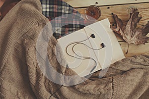 Fall background. Opened book, fall leaf and black earphones on knitted sweater. Knitted scarf on wooden table. Autumn weekend