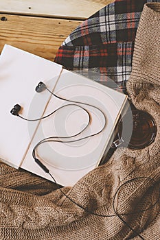 Fall background. Opened book, fall leaf and black earphones on knitted sweater. Knitted scarf on wooden table. Autumn weekend