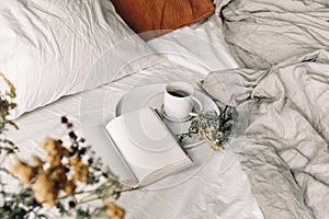 Fall breakfast still life. Cup of coffee, open book and tansy flowers on white linen background. Blurred floral