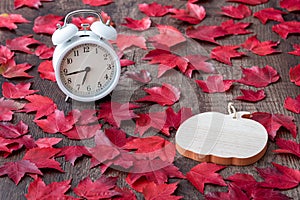 Fall color in red maple leaves on a rustic wood floor with a wood pumpkin and a white analog alarm clock