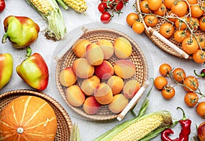 Fall colorful vegetables and fruits set: apricots, tomatoes, paprika, pumpkin, corn, etc. in wicker trays on rustic linen