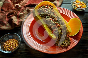 Fall colors with Butternut Squash Boat filled with ground beef with sliced olives on a red plate with some red pepper flakes on t