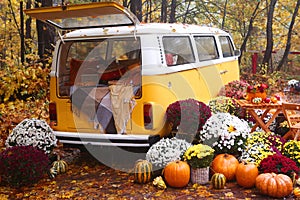 fall composition with old van, pumpkins, flowers and picnic chairs and table on the autumn forest background