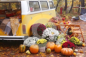 fall composition with old van, pumpkins, flowers and picnic chairs and table on the autumn forest background