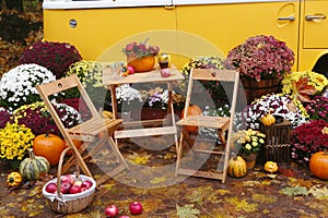 fall composition with old van, pumpkins, flowers and picnic chairs and table on the autumn forest background