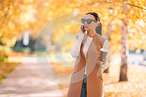 Fall concept - beautiful woman drinking coffee in autumn park under fall foliage