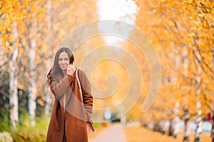 Fall concept - beautiful woman drinking coffee in autumn park under fall foliage