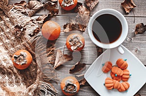 Fall flatlay with checkered plaid, coffee, persimmons, pumpkin candies and dry leaves