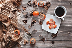 Fall flatlay with checkered plaid, coffee, persimmons, pumpkin candies and dry leaves