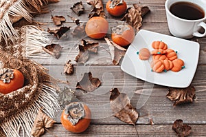 Fall flatlay with checkered plaid, coffee, persimmons, pumpkin candies and dry leaves