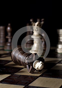 Fall of the king after checkmate at the end of a game on top of a chess board in front of a dark background