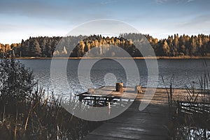 Fall landscape with wood jetty, lake, yellow dark woods on horizon and sky in autumn