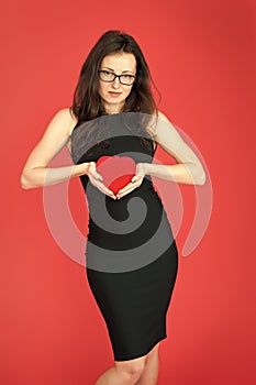 Fall in love. Woman elegant black dress hold heart soft toy. Love from first sight. Woman stylish dress and eyeglasses