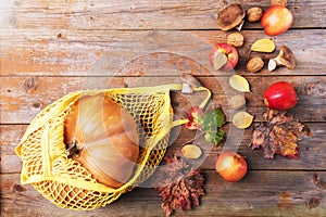 Fall pumpkin in a mesh cotton eco bag with apples, cardoncelli mushrooms, walnuts, leaves on old wooden boards. Autumn shopping,