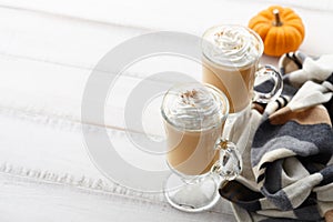 Fall pumpkin spice latte with whipped cream on white wooden background