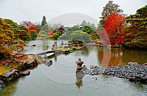 Fall scenery of fiery maple trees by a lake & a stone bridge over the pond on a drizzling day in the beautiful Japanese garden