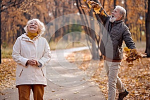 Fall season. Family aged couple throwing leaves in autumn forest, having fun outdoors