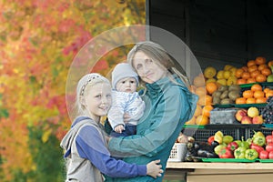 Fall street outdoor family portrait of mother and two siblings at bright fall tree leaves and fruit stand background