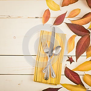 Fall Table Place Setting Invite Card with Brown and Gold Leaves, Silverware, and Napkin Flat Lay on White Shiplap boards backgrou