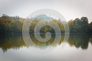 Fall trees and lake reflection on a foggy morning