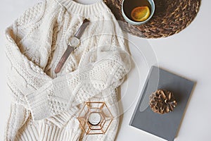 Fall or winter cozy still life set. Warm knitted sweater, cup of tea with lemon, and book with pine cone on white background