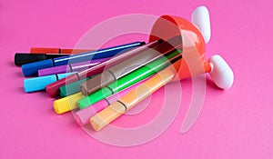 Fallen colored markers and a red stand with white legs isolated on a pink background