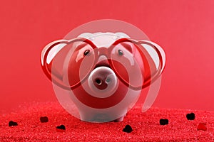 Fallen in love piggy bank with red heart sunglasses standing on red sand with red shining heart glitters in front of red