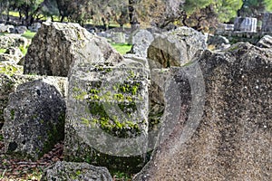 Fallen pieces of classical pillars pitted with age and growing moss at site of ancient Olympia where first Olympics were held in