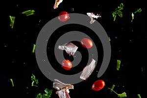 Falling bacon, cherry tomatoes, parsley on a black background with water drops, freeze in motion, cooking and recipe books, banner