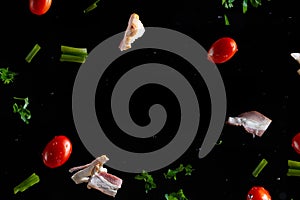 Falling bacon, cherry tomatoes, parsley on a black background with water drops, freeze in motion, frame for an inscription or